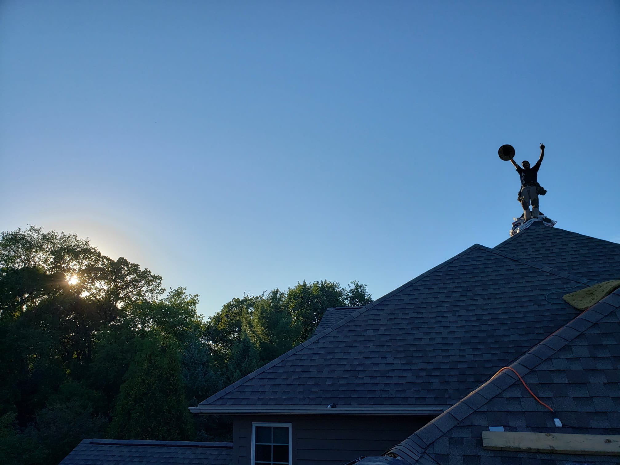 Spider Construction roofer atop a freshly shingled roof at sunset, arms raised, in the Madison, WI area
